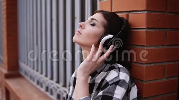 女人沉思地听着耳机里的音乐靠在街边篱笆的墙上我的眼睛视频的预览图