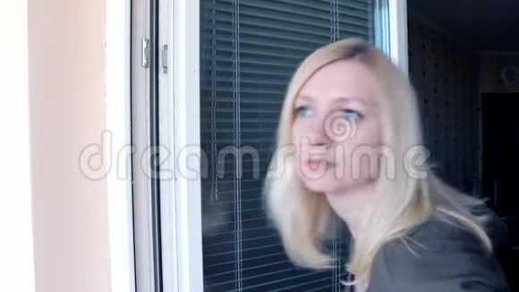 年轻迷人的家庭主妇金发女人站在敞开的窗户附近望着一个人挥舞着她的手视频的预览图