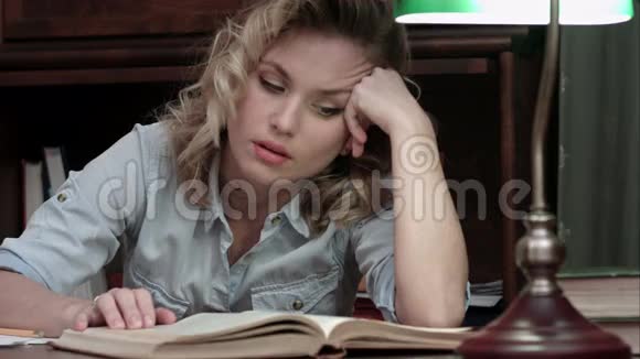劳累了一天的年轻女子在工作后坐在桌子旁看书睡着了视频的预览图
