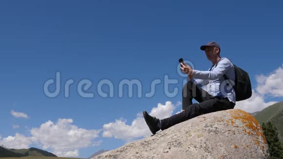 登山时坐在大石头上用手机打视频聊天视频的预览图