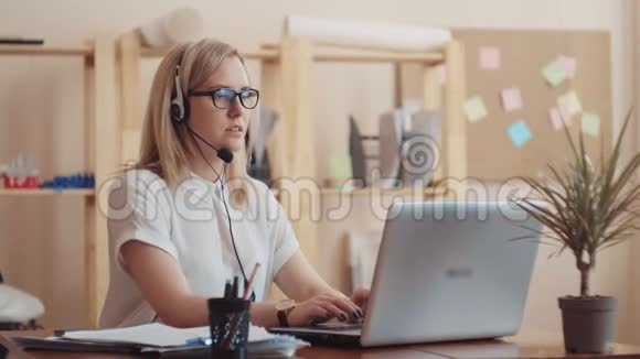 戴眼镜的女孩白种人的外表坐在电脑耳机旁带着麦克风为人们提供建议视频的预览图