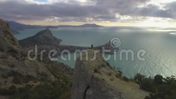 无人机正飞过日出时站在岩石山顶的登山者轮廓视频的预览图