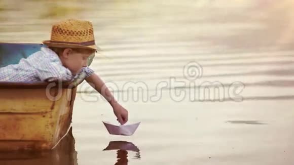 男孩把一艘纸船放在水面上吹着让它飞走视频的预览图