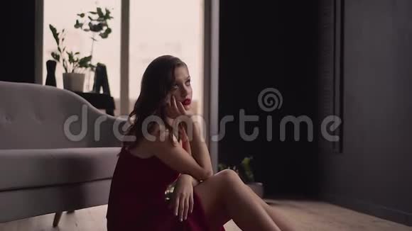 一位身着优雅红色连衣裙的红发美女正坐在地板上视频的预览图