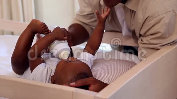 小男孩躺在婴儿床上由父亲喂养视频的预览图