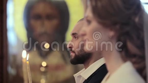 教堂里一对新婚夫妇的特写镜头背景是耶稣基督像上的蜡烛视频的预览图