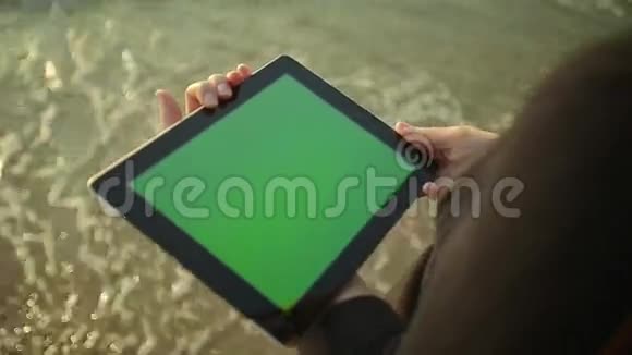 女人在海边的绿色屏幕上使用平板电脑视频的预览图