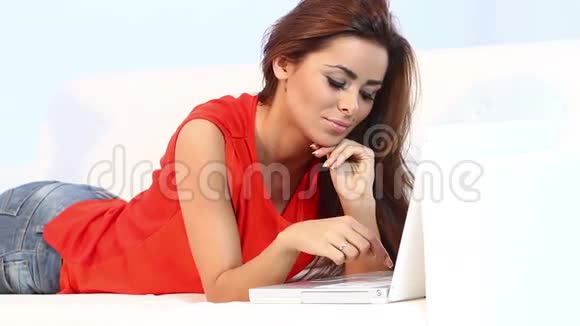漂亮的黑发女人躺在沙发上用电脑工作视频的预览图