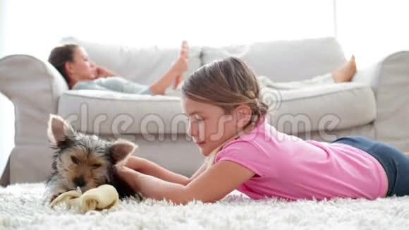 小女孩玩小狗嚼骨头妈妈在沙发上看书视频的预览图