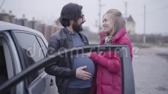微笑白种人金发女人抚摸她丈夫怀孕腹部模仿倾听婴儿撞击快乐视频的预览图