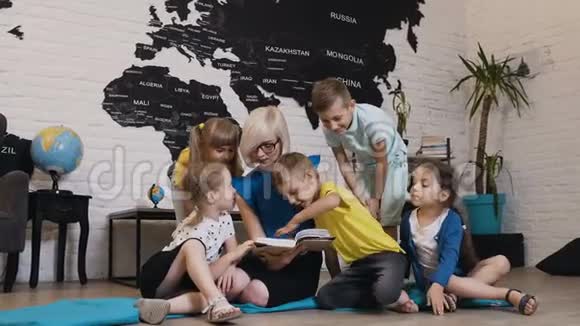 一群漂亮的孩子在幼儿园和幼儿园老师谈论书快乐的儿童日托工作者视频的预览图