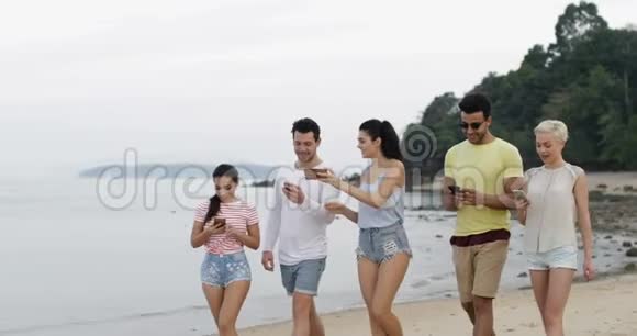 使用手机在线聊天的人们在海滩上行走年轻游客群体视频的预览图