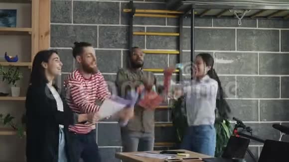 不同群体的女性和男性创业团队在现代办公室里玩有趣的舞蹈派对投掷纸文件视频的预览图