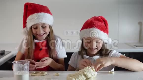 两个可爱的小女孩戴着圣诞老人的帽子围着红色的圣诞围裙亲手做饼干微笑新年快乐视频的预览图