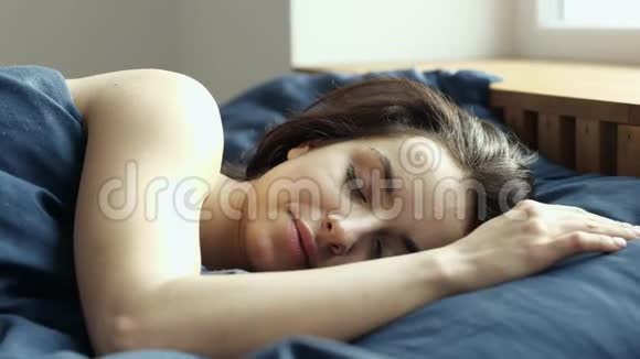 年轻女子在检疫期间呆在家里早上睡在卧室的床上闭着眼睛躺着享受视频的预览图