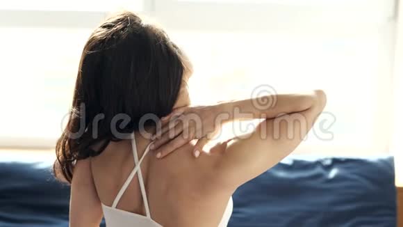 年轻女子在检疫期间呆在家里慢动作坐在前窗用手给她按摩背部伤害和伤害视频的预览图