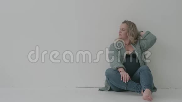坐在白墙旁的大肚子牛仔裤美女孕妇视频的预览图