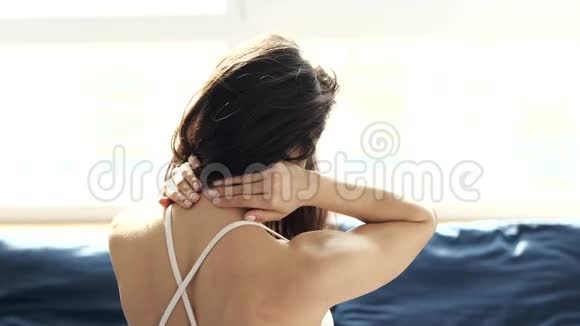 隔离期间年轻女子呆在家里坐在窗前用手按摩颈部身体疼痛视频的预览图