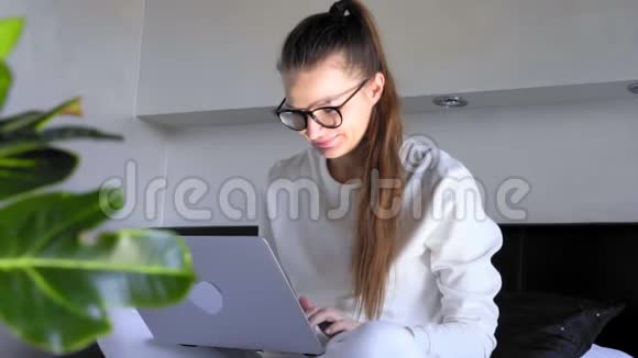 微笑着戴着眼镜的年轻女子在家学习看屏幕上网在笔记本电脑上输入电子邮件辅导自由职业者视频的预览图