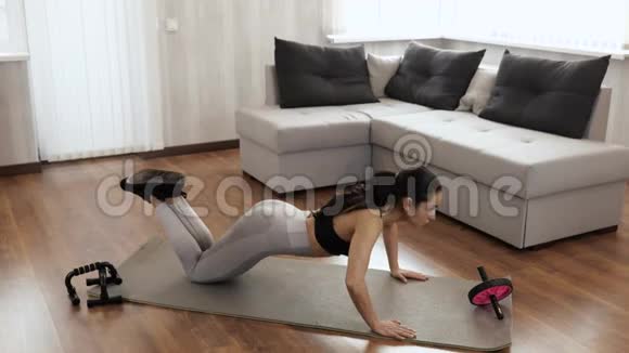 这个年轻女子在隔离期间在家锻炼在地板瑜伽垫上做俯卧撑双膝站立下压视频的预览图