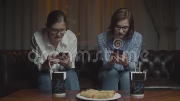 两个戴着智能手机眼镜的女性朋友在深夜坐在沙发上微笑和交谈亚洲盒装食品视频的预览图