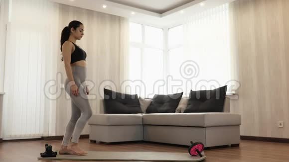年轻女子在隔离期间在家锻炼站直在瑜伽垫上在一个位置上用战士的体式姿势视频的预览图