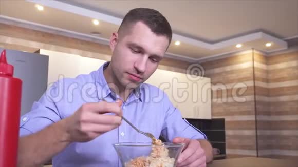 年轻人坐在厨房里吃番茄酱或酱汁的意大利面家伙拿了一些叉子的食物放进嘴里吃东西视频的预览图