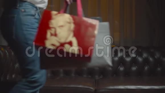 穿牛仔裤的30多岁的女性把购物袋放在桌子上坐在沙发上从沙发上购物的女人那里得到快乐和疲惫视频的预览图