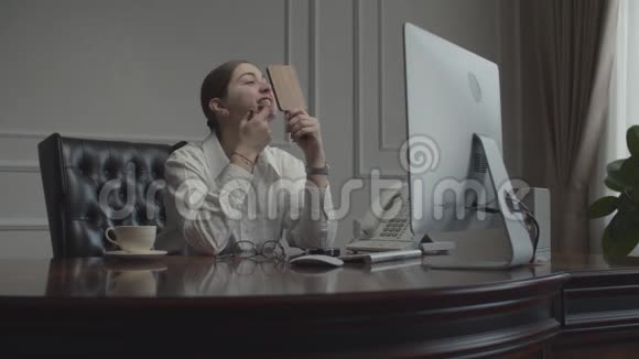 年轻的女商人在工作场所化妆照镜子女性坐在办公桌前电脑显示器在视频的预览图