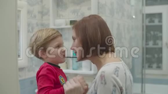 年轻的母亲和穿着红色睡衣的学龄前男孩互相涂抹保湿霜有趣的家庭洗浴常规视频的预览图