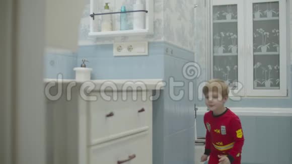 金发的学龄前男孩穿着消防员睡衣跑向水槽拿起牙刷开始在浴室刷牙视频的预览图