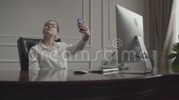 年轻的女商人在办公桌前工作班长坐在商务办公室的扶手椅上女性在智能手机上分心视频的预览图