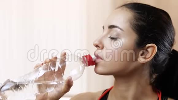 年轻女子在隔离期间在家锻炼独立站立运动后喝水广告水合作用视频的预览图