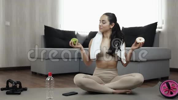 年轻女子在隔离期间在家锻炼绿色健康的苹果和肥美的甜甜圈有三次怀疑视频的预览图