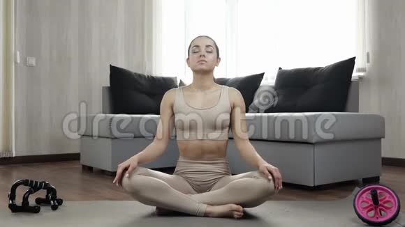 年轻女子在隔离期间在家锻炼在瑜伽垫上以莲花的姿势着色双手并拢放在胸前视频的预览图