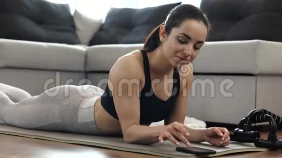 这个年轻女子在隔离期间在家锻炼女性在智能手机上打开秒表站在木板上视频的预览图
