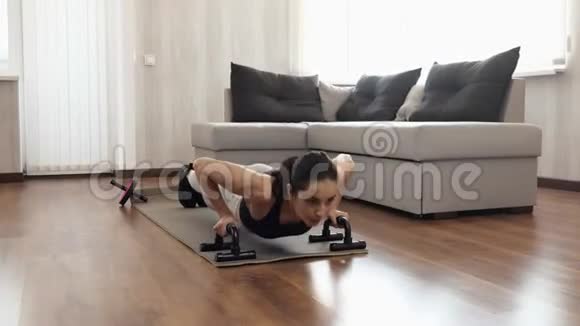 年轻女子在隔离期间在家锻炼主动俯卧撑与哑铃在瑜伽垫使手臂更强壮视频的预览图
