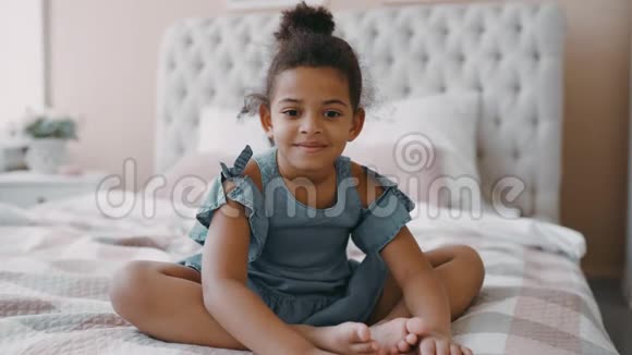 美丽快乐微笑美国女孩卷发坐在舒适的卧室里穿着蓝色的印花裙视频的预览图