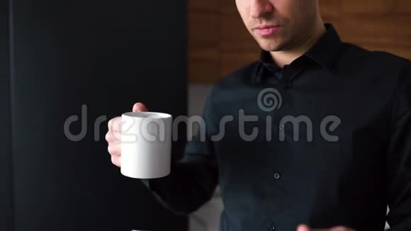 年轻成功的布尼斯曼在黑色衬衫喝热饮和使用平板电脑的视频从家里远程工作照相机视频的预览图