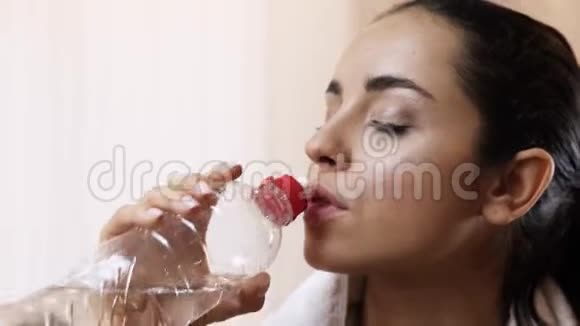 年轻女子在隔离期间在家锻炼女孩在训练后从瓶子里喝水水合作用视频的预览图