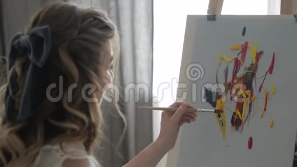 一个年轻的女孩在画布上画画微笑着喜欢画画的过程视频的预览图