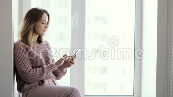 女人浏览手机坐在窗户上人类使用手机视频的预览图