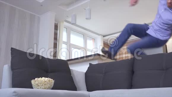 兴奋的积极的年轻人跳上沙发看电视连续剧拿着爆米花碗打开视频激动的情绪视频的预览图
