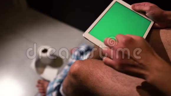 男人坐在马桶或锅上手里拿着绿色屏幕的平板电脑的视频刷了好几下滚动视频的预览图