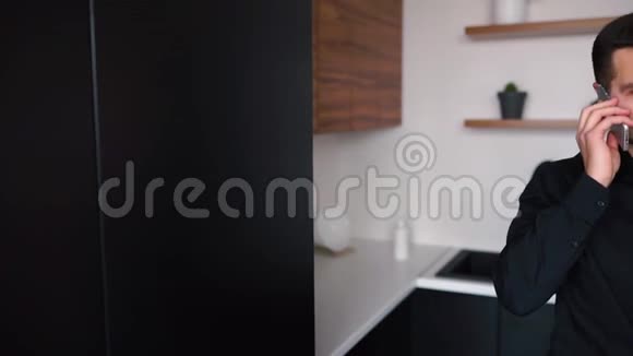 迷人的忙碌的年轻商务人员在电话和使用平板电脑远程工作单独站在厨房里商务视频的预览图
