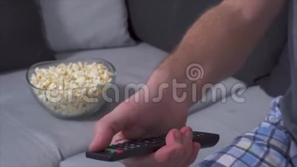 男子手持电视遥控器并按下遥控器上的按钮的特写镜头切换电视频道爆米花碗视频的预览图
