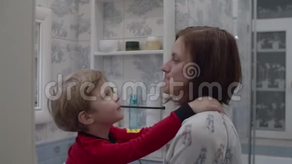 年轻的母亲和穿着红色睡衣的儿子在浴室里拥抱和笑有趣的家庭沐浴常规孩子吻妈妈视频的预览图