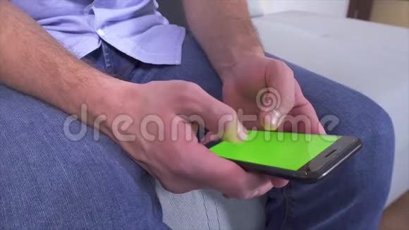 男人坐着手里拿着智能手机的观点利用它设备上的绿色屏幕输入电子键盘及视频的预览图