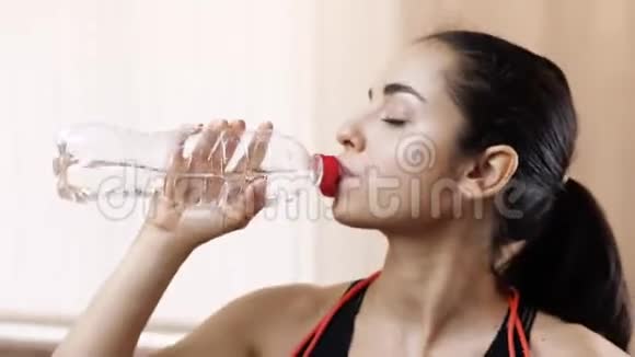 年轻女子在隔离期间在家锻炼苗条的女孩运动后从瓶子里喝水满意视频的预览图