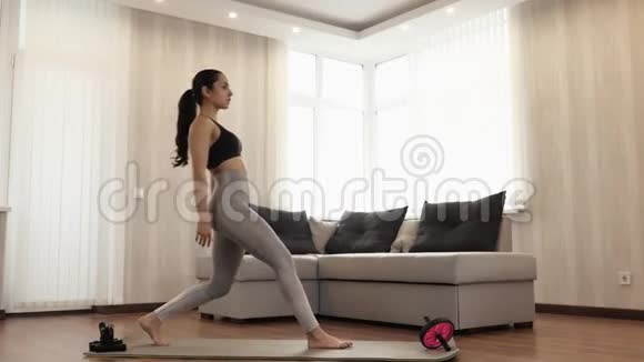 年轻女子在隔离期间在家锻炼苗条女性站在单腿下蹲运动和站立别动视频的预览图